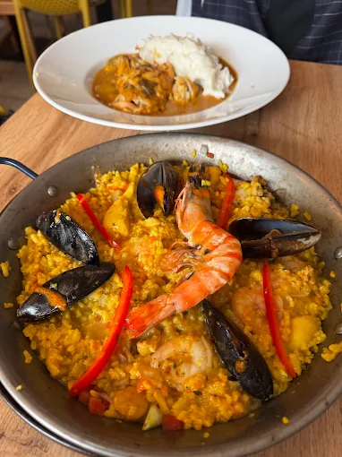 Paella mit Garnelen, Muscheln und Paprika in der Pfanne, dazu ein Beilagenteller
